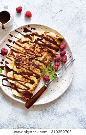 Crepe With Chocolate Paste, Banana And Raspberries On A Concrete Background. Tasty Breakfast.