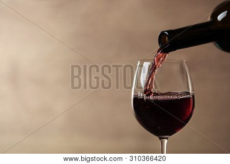 Pouring Red Wine Into Glass From Bottle Against Blurred Beige Background, Closeup. Space For Text