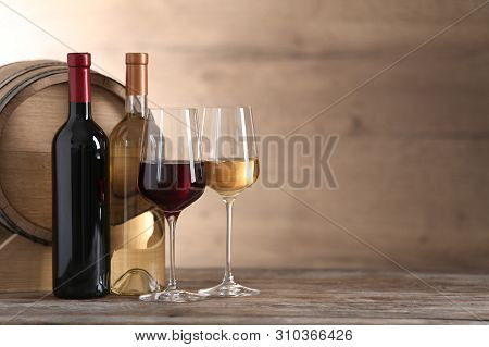 Glasses And Bottles Of Different Wine Near Wooden Barrel On Table. Space For Text