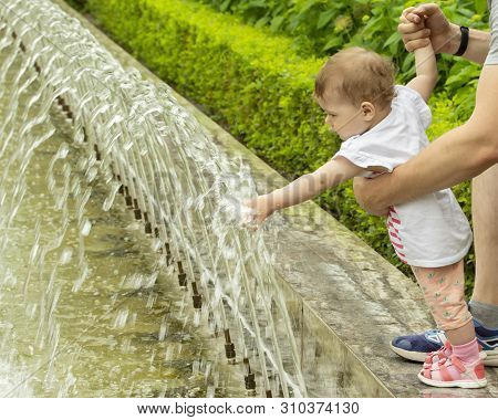 Baby Pink Sandals Playing With Water. The Baby Touches The Water In The Fountain, Shoves Hands Under