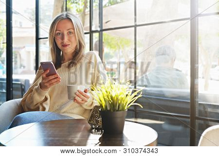 Alone Time In Coffee Shop. Young Beautiful Woman Wearing Off Shoulder Sweater Having Cup Of Hot Beve