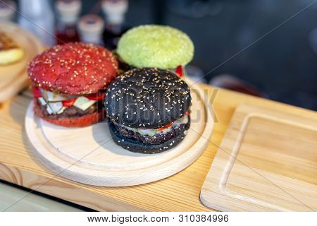 Three Tasty Bright Multicolored Beef Burgers On Wooden Counter At Food Fest. Amburger Bun Clolred Wi