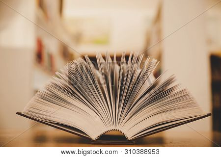 Opened Book On The Desk And Isle Of Bookshelves In School Study Class Room Background For Academic E