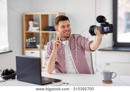 blogging, videoblog and people concept - smiling male video blogger with camera videoblogging and shoeing peace hand sign at home office