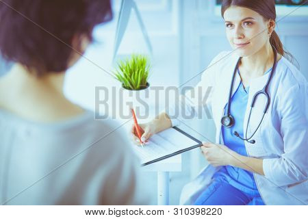 Doctor and patient discussing medical problems in a hospital consulting room. Doc filling in a patient's form
