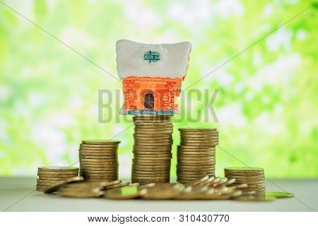 Mini House On Stack Of Coins With Green Blur Background.