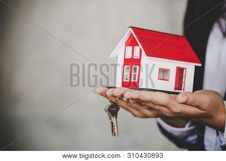 Agent Businessman In White Shirt Holding Keys In Hand A Small House And Apartment