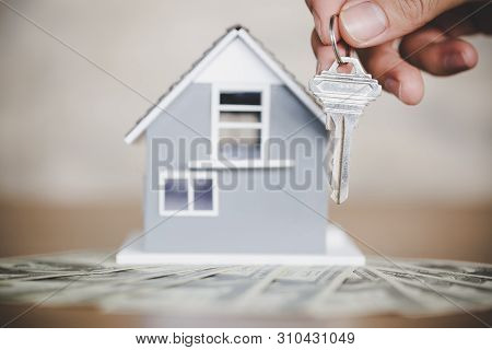 Little House Toy And One Hundred Dollar Bills On Table With A Key In Woman Hands