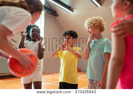 Children Smiling To Their Sports Teacher In The Gym.