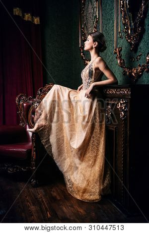 A full length portrait of a mysterious lady in a fluffy long dress posing in the interior. Interior, fashion.