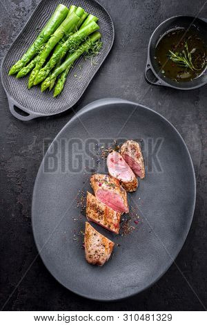 Fried Iberian pork fillet sliced with blanched green asparagus and butter sauce with spice as top view in a cast iron design plate 