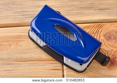 Office Paper Hole Puncher. Blue Paper Hole Puncher On Wooden Background. Metal Stationery Accessory.