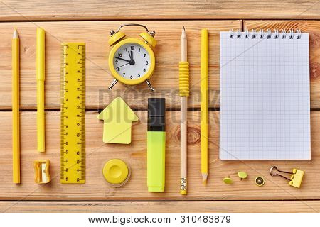 Student Accessories On Wooden Background. Flat Lay Blank Paper Notebok And Set Of Yellow School Supp