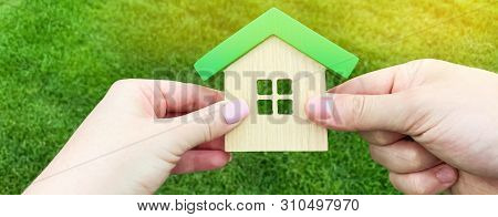 Wooden House In The Hand Of A Young Family. Buying A Home In A Mortgage Loan. Real Estate Concept. E