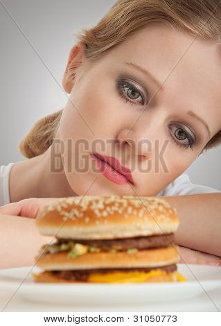 Krásná dívka sedí na dietě, smutno při pohledu na Hamburger