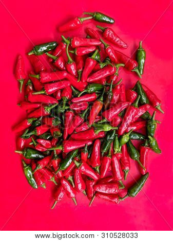 Red And Green Chilli Peppers. Large Fresh Pile On A Red Background. Overhead View. Vertical.
