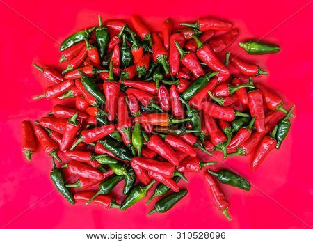 Red And Green Chilli Peppers. Large Fresh Pile On A Red Background. Overhead View.