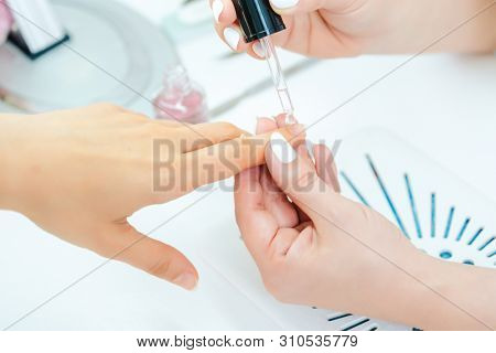 Manicurist pouring essential oil on finger nails of woman after pedicure