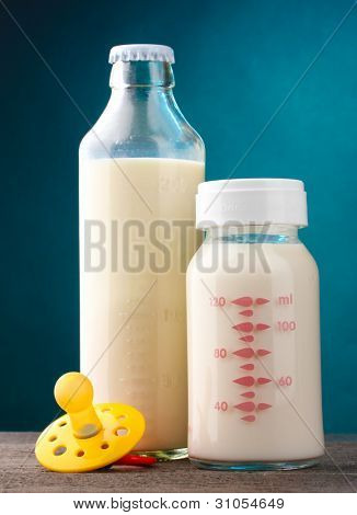 Flaschen Milch und Schnuller auf Holztisch auf blauem Hintergrund