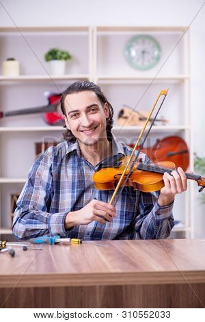 Young handsome repairman repairing violin