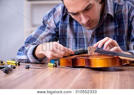 Young handsome repairman repairing violin