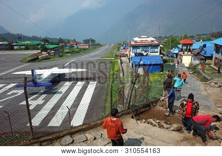 Lukla, Nepal - May 8, 2019: Nepali workers paving walkway next to fence of TenzingâHillary airport in Himalayas mountains