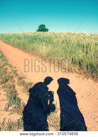 People Shadows On Old Dusty Road With Ferric Red Soil.  Shadows Of Walking Pedestrians Projected On 