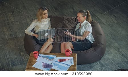 Two Beautiful Business Woman In Skirts Resting On The Couch, Holding A Laptop Girl, The Other Girl T