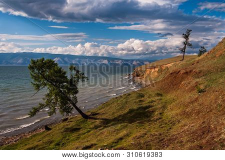 Lake Baikal With Mountains In The Background And Beautiful Clouds And Light. Trees With Shadow On Th