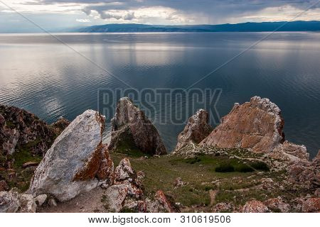 Beautiful Large Stones On The Background Of Lake Baikal. On The Stones Is Red Moss. In The Sky Cloud