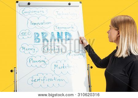 Side View Of Businesswoman Standing Near White Flipchart, Pointing At Words On Flipchart