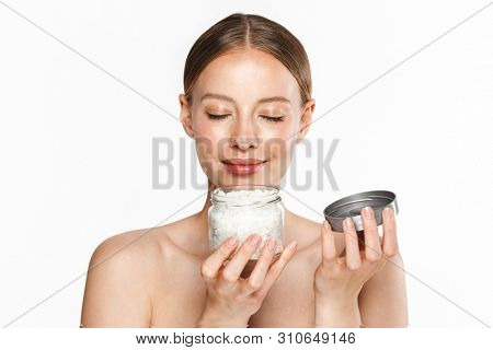 Image of young half-naked woman smelling bath salt from jar with closed eyes isolated over white background