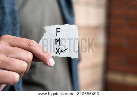 closeup of a young caucasian person holding a piece of paper with the letters F for female, M for male and X for the third gender category, written in it, with a check mark on the X