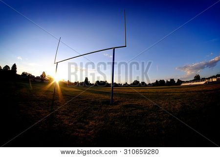Football goalposts goal posts uprights at sunset with sun sky and bleachers