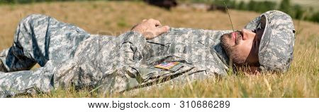 Panoramic Shot Of Cheerful Soldier In Military Uniform Lying On Grass