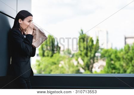 Young Businesswoman Standing On Rooftop And Breathing Into Paper Bag While Suffering From Panic Atta