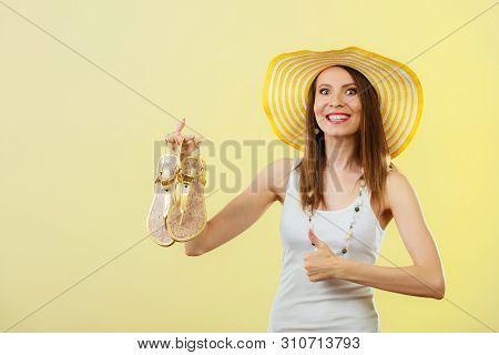 Holidays Summer Fashion Concept. Woman In Big Yellow Hat Holding Golden Sandals In Hand Bright Backg