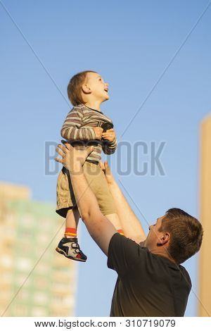 Father And Son Having Fun Together Outdoors.dad Tossing Son Up Against Blue Sky.  Vertcal Shot