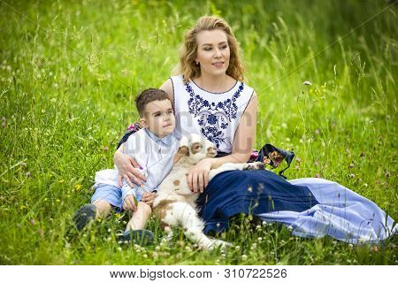 Mother Along With Her Little Son And Cub Of Newborn Lamb Posing Outdoors On Nature Background. Horiz