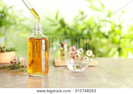 Dripping Natural Tea Tree Essential Oil Into Bottle On Table, Space For Text
