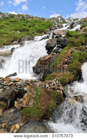 Predatory Mountain River In The Mountains Of The Taur Alps, Green Pasture With Blue Sky, Austria