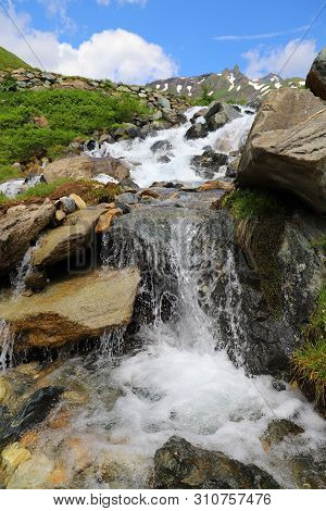 Predatory Mountain River In The Mountains Of The Taur Alps, Green Pasture With Blue Sky, Austria