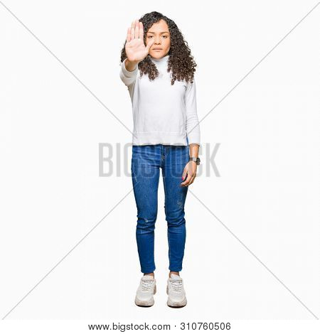 Young beautiful woman with curly hair wearing turtleneck sweater doing stop sing with palm of the hand. Warning expression with negative and serious gesture on the face.