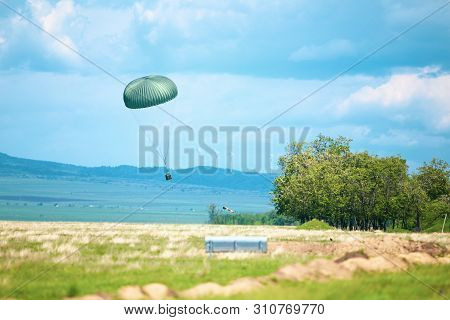 A Military Crate Is Being Parachuted From A Military Cargo Plane During A Drill.
