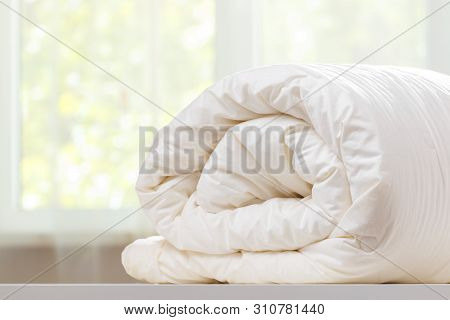 A Folded Rolls Duvet Is Lying On The Dresser Against The Background Of A Blurred Window. Household.