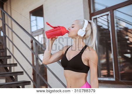 A Young Athletic Woman In White Headphones Working Out Listening To The Music On A Stairs Outdoors. 