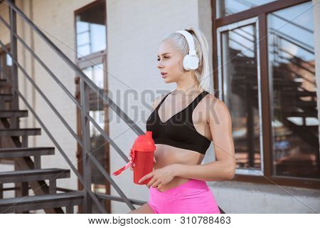 A Young Athletic Woman In White Headphones Working Out Listening To The Music On A Stairs Outdoors. 