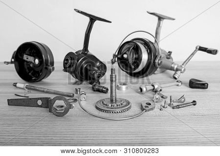 A Fishing Spinning Reel As A Whole And A Second Similar Completely Disassembled. Black And White Ima