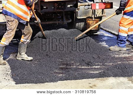 The Working Crew Evenly Distributes Hot Asphalt With Shovels Manually On The Repaired Site Of The Ro
