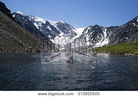 Young Man Swimming In A Mountain Lake On Background Of Beautiful Mountain Landscape With Snow-capped